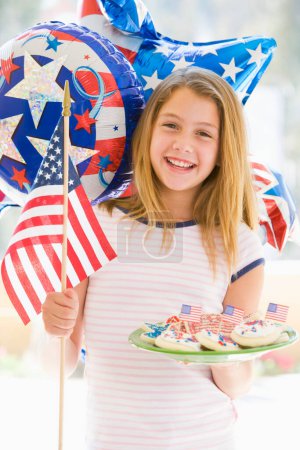Téléchargez les photos : "Jeune fille à l'extérieur le 4 juillet avec drapeau et biscuits souriants" - en image libre de droit