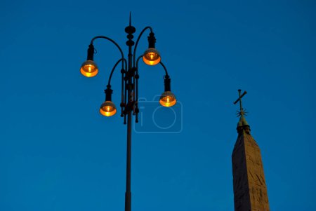 Téléchargez les photos : Lampadaire et sur le dessus de l'église avec croix sur fond bleu ciel - en image libre de droit
