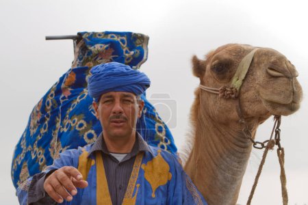 Foto de Man in traditional Moroccan costume with camel in the desert - Imagen libre de derechos