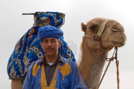 Photo for Man in traditional Moroccan costume with camel in the desert - Royalty Free Image