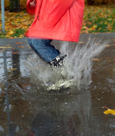 Photo for Woman jumping in puddle during Rainy weather - Royalty Free Image