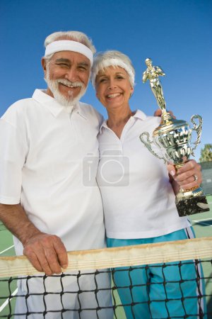 Foto de "Retrato de feliz pareja mayor sosteniendo trofeo en la red de tenis
" - Imagen libre de derechos
