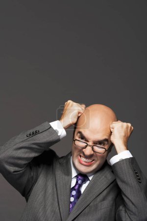 Téléchargez les photos : Homme d'affaires chauve avec poings frappant tête chauve sur fond gris - en image libre de droit