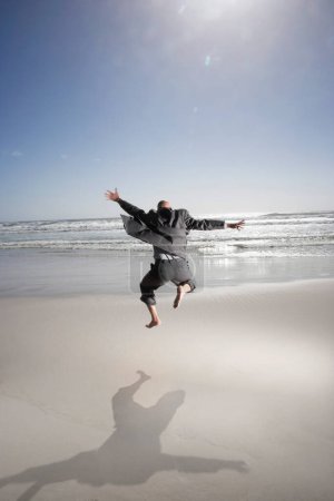 Téléchargez les photos : Vue arrière d'un homme d'affaires d'âge moyen sautant sur la plage - en image libre de droit