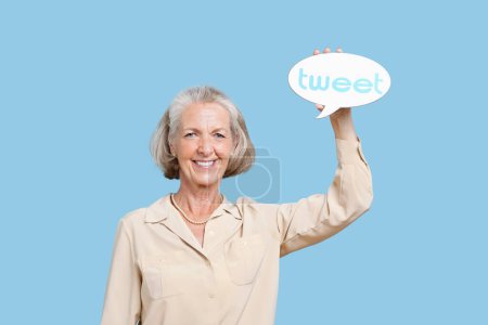 Téléchargez les photos : Portrait d'une femme âgée tenant une bulle de tweet sur fond bleu - en image libre de droit