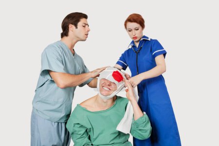 Téléchargez les photos : Médecin masculin avec infirmière pansant un patient blessé sur fond gris - en image libre de droit