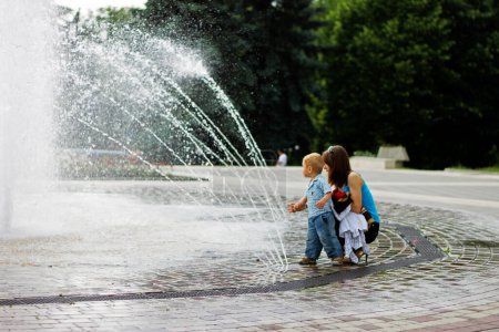 Téléchargez les photos : Femme et enfant marchant autour de la fontaine éclaboussante dans le centre o" - en image libre de droit