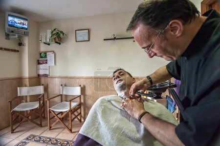 Téléchargez les photos : "Barbier rasage avec un rasoir pour jeune homme dans un salon de coiffure, Sab" - en image libre de droit