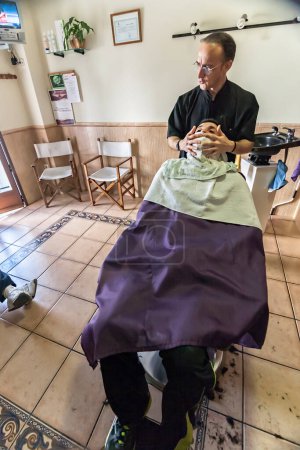 Photo for Barber applies a hot water cloth in the face of the client - Royalty Free Image