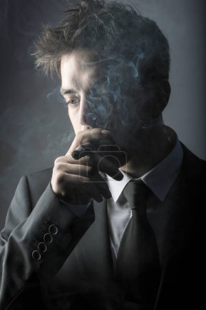 Téléchargez les photos : Jeune homme élégant fumant un cigare en studio - en image libre de droit