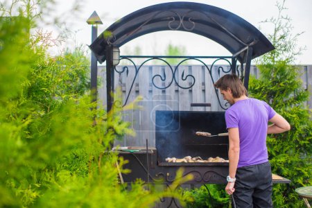 Téléchargez les photos : "Jeune homme frites steaks sur le gril en plein air dans sa cour
" - en image libre de droit
