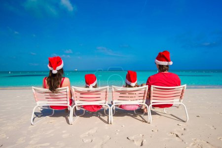 Photo for Happy family of four on beach in red Santa hats - Royalty Free Image