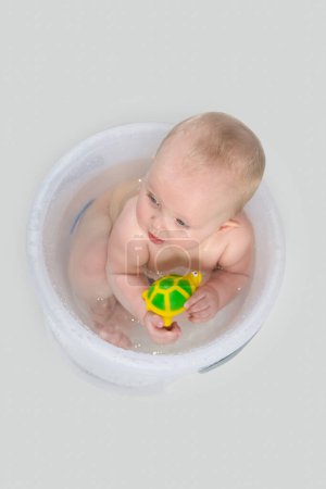 Téléchargez les photos : Bébé mignon ayant un bain dans un seau transparent et jouant - en image libre de droit