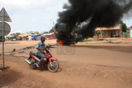 Foto de BURKINA FASO, Ouagadougou: Un hombre en una motocicleta conduce frente a un neumático en llamas cerca del palacio presidencial en Ouagadougou, Burkina Faso, el 18 de septiembre de 2015. - Imagen libre de derechos
