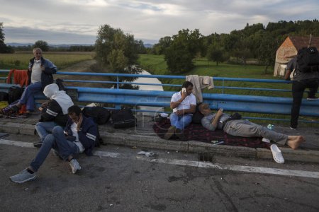Téléchargez les photos : CROATIE, Harmica : Les réfugiés se tiennent debout et attendent sur un pont dans le village de Harmica, en Croatie, à la frontière de la Slovénie, le 19 septembre 2015, après que le gouvernement slovène a empêché les réfugiés d'entrer dans le pays avec la police anti-émeute. - en image libre de droit