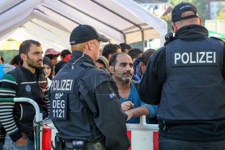 Foto de Alemania, Passau: Funcionarios de seguridad hacen guardia mientras los refugiados esperan en largas colas en la ciudad fronteriza de Passau, Alemania, el 21 de septiembre de 2015 - Imagen libre de derechos