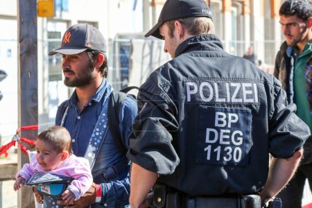 Téléchargez les photos : Allemagne, Passau : Des responsables de la sécurité montent la garde alors que les réfugiés attendent dans de longues files d'attente dans la ville frontalière de Passau, en Allemagne, le 21 septembre 2015 - en image libre de droit