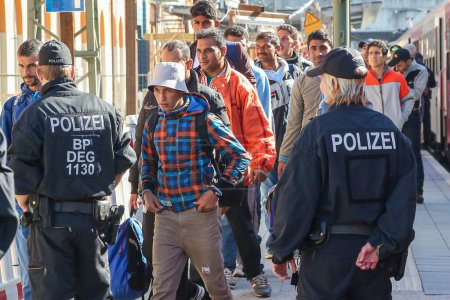 Téléchargez les photos : Allemagne, Passau : Des responsables de la sécurité montent la garde alors que les réfugiés attendent dans de longues files d'attente dans la ville frontalière de Passau, en Allemagne, le 21 septembre 2015 - en image libre de droit