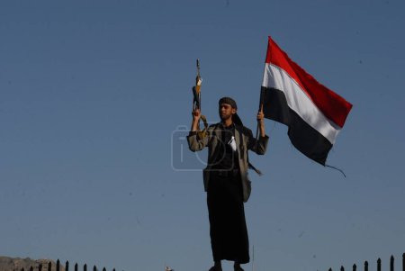 Téléchargez les photos : YEMEN, Sanaa : Un sympathisant chiite-houthis tient un drapeau yéménite et lève son fusil lors d'une manifestation à Sanaa le 2 octobre 2015, contre les opérations militaires en cours menées par la coalition dirigée par l'Arabie saoudite. - en image libre de droit