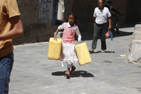 Téléchargez les photos : YEMEN, Taiz : Une jeune fille yéménite transporte des jerrycans pour les remplir d'eau lors d'une distribution de nourriture et d'eau potable à l'école de Nasser, près de Taiz (Ta'izz), dans l'ouest du Yémen, le 23 octobre 2015 - en image libre de droit
