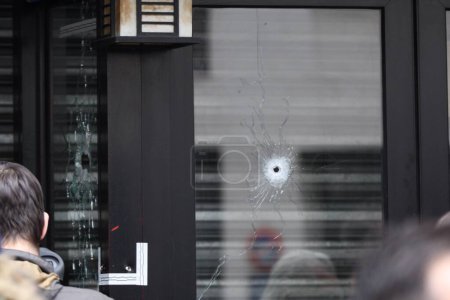 Foto de FRANCIA, París: La gente mira agujeros de bala que dañaron una ventana de una pastelería en la rue de Charonne, en el distrito 11 de París, el 14 de noviembre de 2015 - Imagen libre de derechos