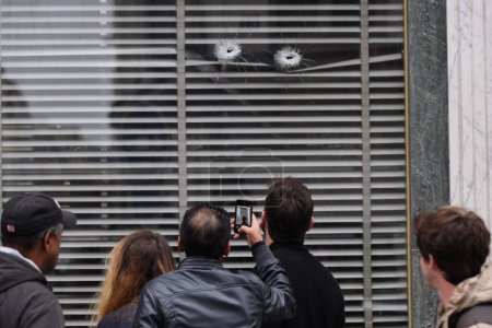 Foto de FRANCIA, París: La gente mira agujeros de bala que dañaron una ventana de una pastelería en la rue de Charonne, en el distrito 11 de París, el 14 de noviembre de 2015 - Imagen libre de derechos