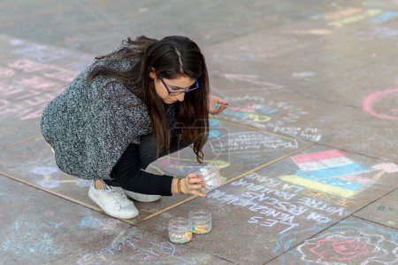 Foto de FRANCIA, Toulouse: Una joven dibuja en el suelo con palos de tiza para rendir homenaje a las víctimas de los ataques de noviembre-13 en París, en la plaza del Capitolio, en Toulouse, al sur de Francia, el 17 de noviembre de 2015. - Imagen libre de derechos