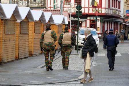 Photo for BELGIUM, Brussels: Two soldiers pass by christmas market small shops (christmas market is in preparation, not yet opened) at the Beurs - Bourse , on November 22, 2015 in Brussels. - Royalty Free Image