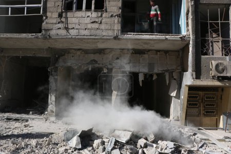 Foto de SIRIA, Saqba: Un residente de la ciudad de Saqba limpia un edificio destruido de la ciudad de East suburbio de Damasco, la capital de Siria, el 28 de diciembre de 2015. - Imagen libre de derechos