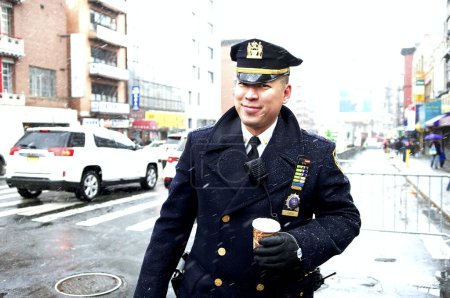 Téléchargez les photos : États-Unis, New York : Un officier sourit alors qu'il se réjouit de la danse Chinatown de New York avec des dragons et marche à travers une neige légère le 8 février 2016 pour célébrer le Nouvel An lunaire. - en image libre de droit