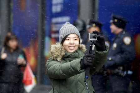 Téléchargez les photos : États-Unis, New York : Une femme prend un selfie en tant que fêtards dans la danse Chinatown de New York avec des dragons et marche à travers une neige légère le 8 février 2016 pour célébrer le Nouvel An lunaire. - en image libre de droit