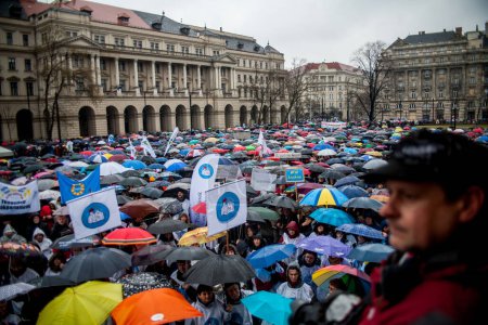 Téléchargez les photos : HONGRIE, Budapest : Les participants à une manifestation pour les enseignants, les parents et leurs sympathisants tiennent des banderoles et des parapluies devant le bâtiment du Parlement à Budapest le 13 février 2016 - en image libre de droit