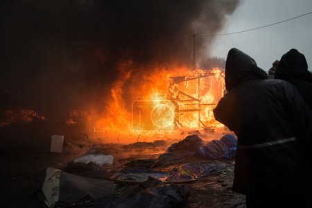 Téléchargez les photos : FRANCE, Calais : Des migrants passent devant une cabane incendiée, dans la partie sud du camp de migrants de la jungle, alors que la moitié du camp est démantelée, dans la ville portuaire française du nord de Calais, le 1er mars 2016 - en image libre de droit