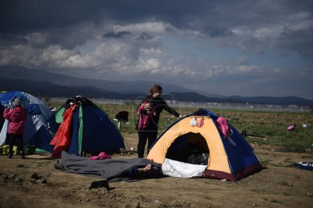 Foto de GRECIA, Idomeni: Los refugiados se reúnen en las vías del ferrocarril en la frontera greco-macedonia cerca de la aldea griega de Idomeni, donde miles de refugiados y migrantes están atrapados por el bloqueo fronterizo de los Balcanes, el 9 de marzo de 2016 - Imagen libre de derechos