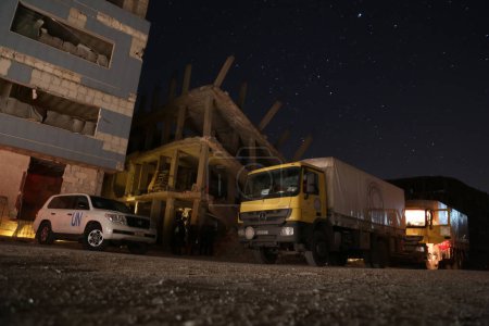 Téléchargez les photos : SYRIE, Saqba : Un camion, qui fait partie d'un convoi tant attendu des Nations Unies, se trouve à côté d'un bâtiment en feu à Saqba, juste à l'est de Damas, en Syrie, le 4 mars 2016. - en image libre de droit