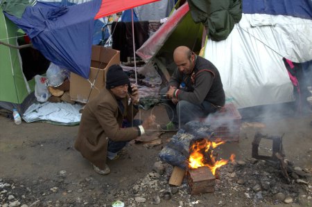 Foto de GRECIA, Idomeni: Los migrantes se calientan por una hoguera en la frontera greco-macedonia cerca de la aldea griega de Idomeni el 10 de marzo de 2016 - Imagen libre de derechos