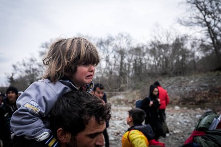 Foto de Grecia, Idomeni - 14 de marzo de 2016: Migrantes y refugiados cruzan un río en ascenso camino a Macedonia desde un campamento improvisado en la frontera greco-macedonia, cerca de la aldea griega de Idomeni - Imagen libre de derechos