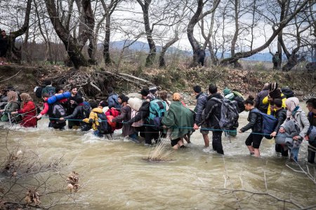 Photo for Greece, Idomeni - March 14, 2016: Migrants and refugee cross a surging river on their way to Macedonia from a makeshift camp at the Greek-Macedonian border, near the Greek village of Idomeni - Royalty Free Image