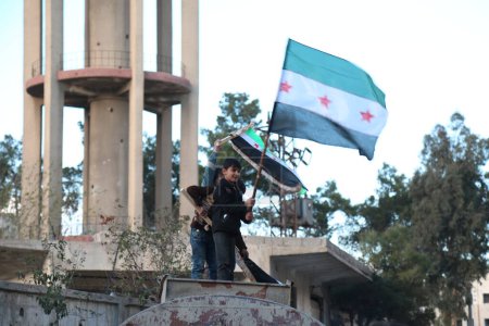 Foto de SIRIA, Saqba: Cientos de sirios portan una bandera siria pre-baaz, que fue adoptada por la revolución siria durante el levantamiento, el 16 de marzo de 2016 en Saqba - Imagen libre de derechos