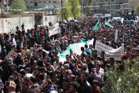 Foto de SIRIA, Saqba: Manifestantes sostienen banderas sirias pre-baaz, adoptadas durante el levantamiento en 2011, y pancartas durante una manifestación contra el régimen en la ciudad rebelde de Saqba, en las afueras de la capital siria, Damasco, el 18 de marzo de 2016. - Imagen libre de derechos