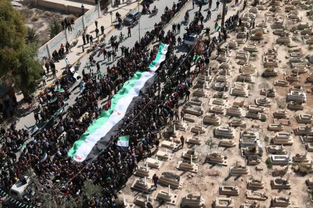 Foto de SIRIA, Saqba: Manifestantes sostienen banderas sirias pre-baaz, adoptadas durante el levantamiento en 2011, y pancartas durante una manifestación contra el régimen en la ciudad rebelde de Saqba, en las afueras de la capital siria, Damasco, el 18 de marzo de 2016. - Imagen libre de derechos