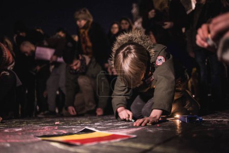 Téléchargez les photos : FRANCE, Paris: A boy draws on the floor with a piece of chalk as people gather in front of the Hotel de Ville, in Paris, as a tribute to the victims of Brussels following triple bomb attacks in the Belgian capital - en image libre de droit