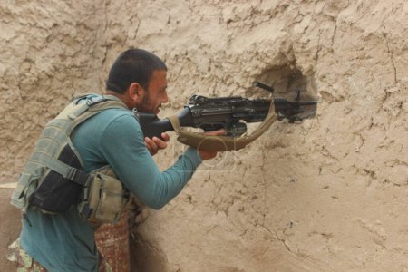 Téléchargez les photos : AFGHANISTAN, Alchin: A man fires behind a wall as soldiers of Afghan national army (ANA) fights back Taliban militants in Alchin village, in Kunduz province, in northern Afghanistan on April 16, 2016. - en image libre de droit