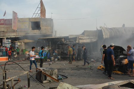 Téléchargez les photos : IRAQ, BAGHDAD - 25 AVRIL 2016 : Des personnes se rassemblent dans un district musulman à majorité chiite de l'est de Bagdad alors que les forces de sécurité et les pompiers irakiens sécurisent le site d'un attentat suicide revendiqué par le groupe État islamique dans la région de New Bagdad - en image libre de droit