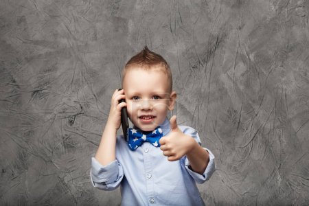 Photo for Portrait of a cute little boy in blue shirt and bow tie with mobile - Royalty Free Image