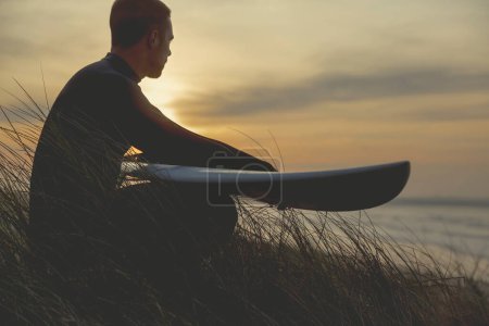 Téléchargez les photos : Surfeur masculin sur le rivage au coucher du soleil - en image libre de droit