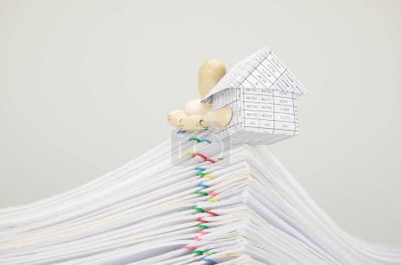Téléchargez les photos : Mannequin en bois tenant la maison sur le dessus des documents de surcharge de pile - en image libre de droit