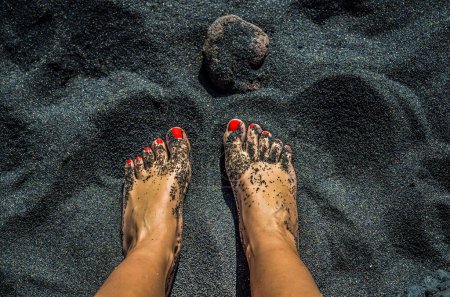 Téléchargez les photos : Femme pieds nus avec des ongles rouges sur la plage de sable noir - en image libre de droit