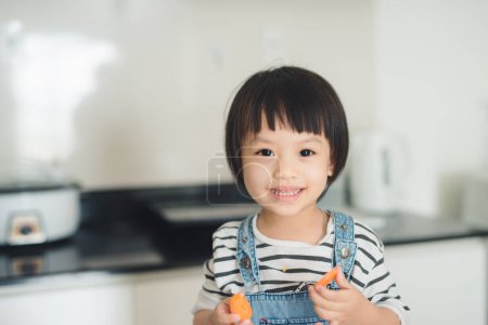 Photo for Child girl having fun with carrot. Home kitchen interior - Royalty Free Image