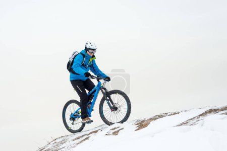 Téléchargez les photos : Cycliste au repos bleu avec VTT sur une colline d'hiver rocheuse. Concept de vélo sport extrême et enduro. - en image libre de droit